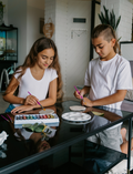 The Express Yourself Program by Therapy At Home features a teal and purple box with paint, markers, brushes, worksheets, bead kit, colored paper, a white cap, and a paint palette—perfect for occupational therapy activities.