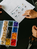 The Express Yourself Program by Therapy At Home features a teal and purple box with paint, markers, brushes, worksheets, bead kit, colored paper, a white cap, and a paint palette—perfect for occupational therapy activities.