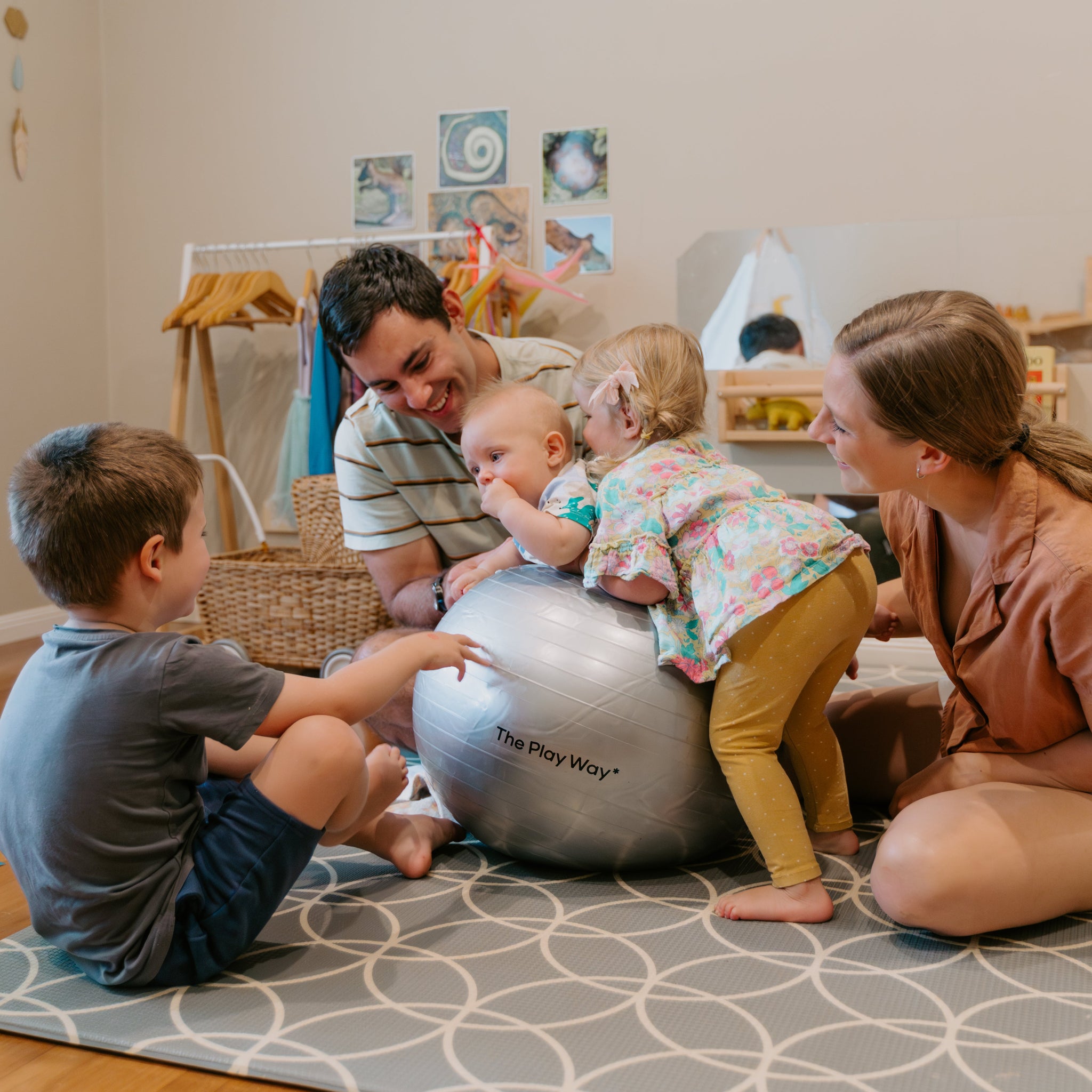 Family playing with a large ball on a patterned rug in a home setting.