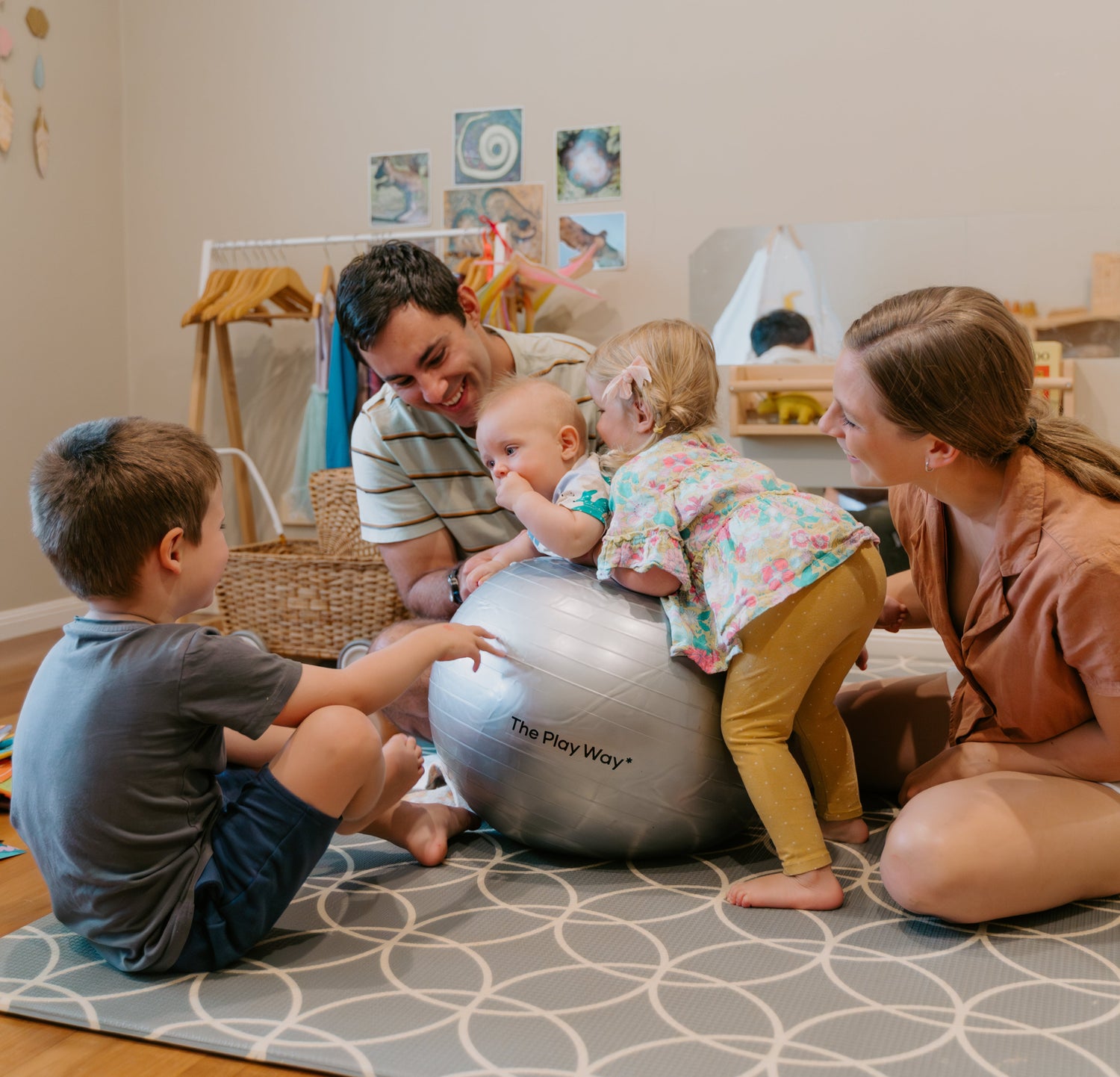 Family playing with a large ball on a patterned rug in a home setting.