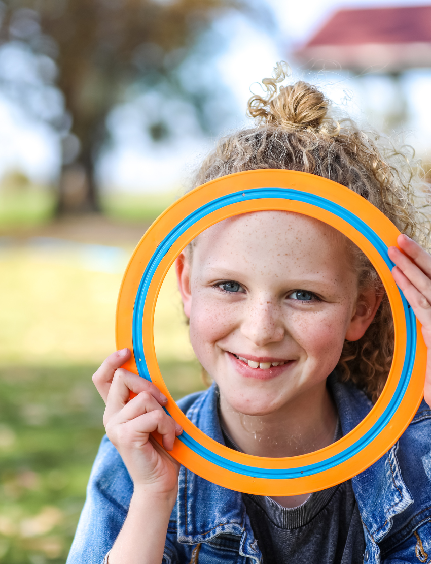 Happy child playing with The Play Way frisbee, part of the Outdoor Action Bundle, for engaging outdoor activities.