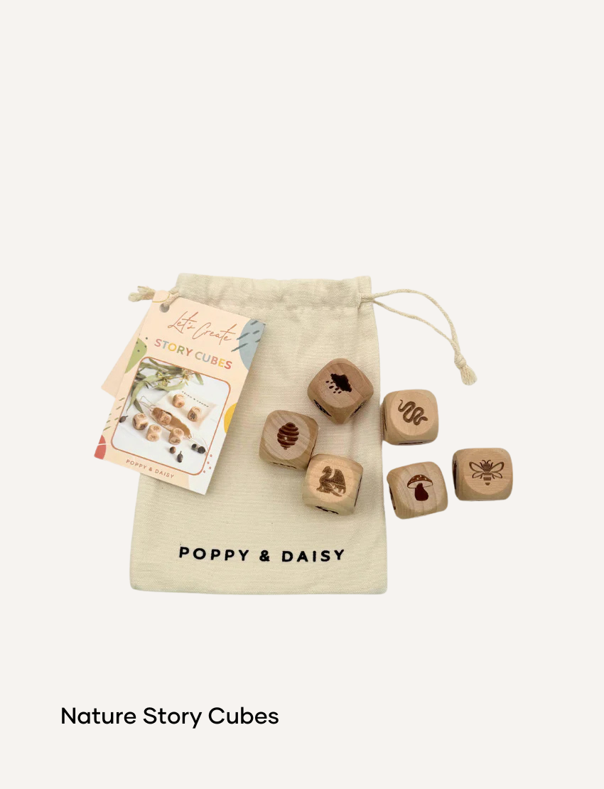 A hand holds a small tin of Lavender Lip Balm. Below it, a cloth pouch labeled "Poppy & Daisy" contains a glass vial, a small wooden stick, and a card with floral illustrations. The background reveals a knitted blanket.