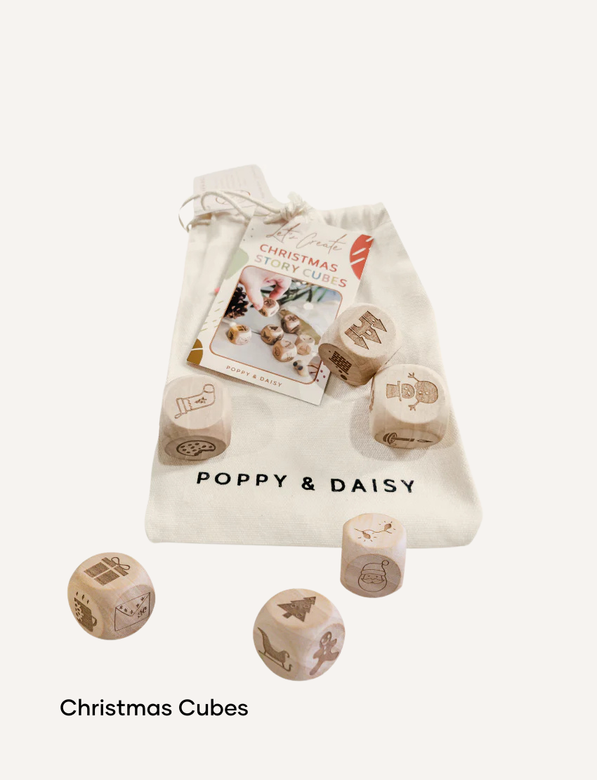 A hand holds a small tin of Lavender Lip Balm. Below it, a cloth pouch labeled "Poppy & Daisy" contains a glass vial, a small wooden stick, and a card with floral illustrations. The background reveals a knitted blanket.