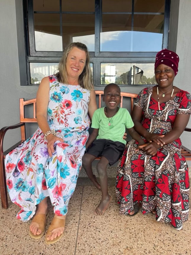 A woman and a child sit on a bench with another woman, smiling, showcasing a connection likely related to charity.