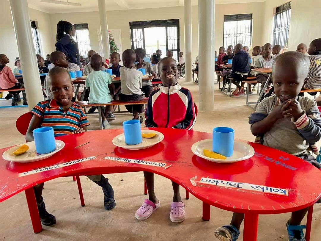Smiling children at red tables in a classroom or dining hall, enjoying a meal together. Happy kids sharing food.