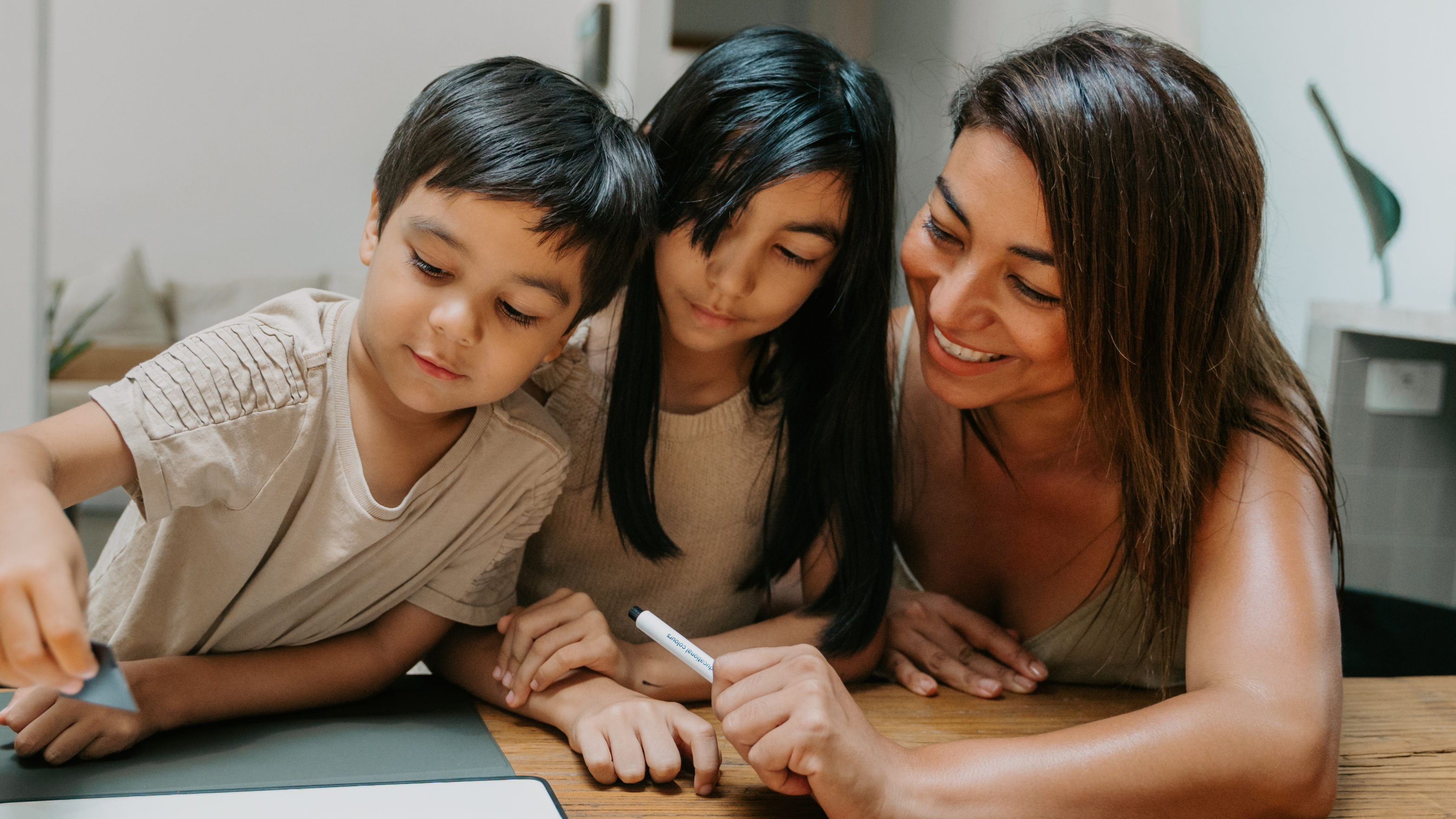 Woman and two children sitting at a table with a tablet, engaged in an activity.