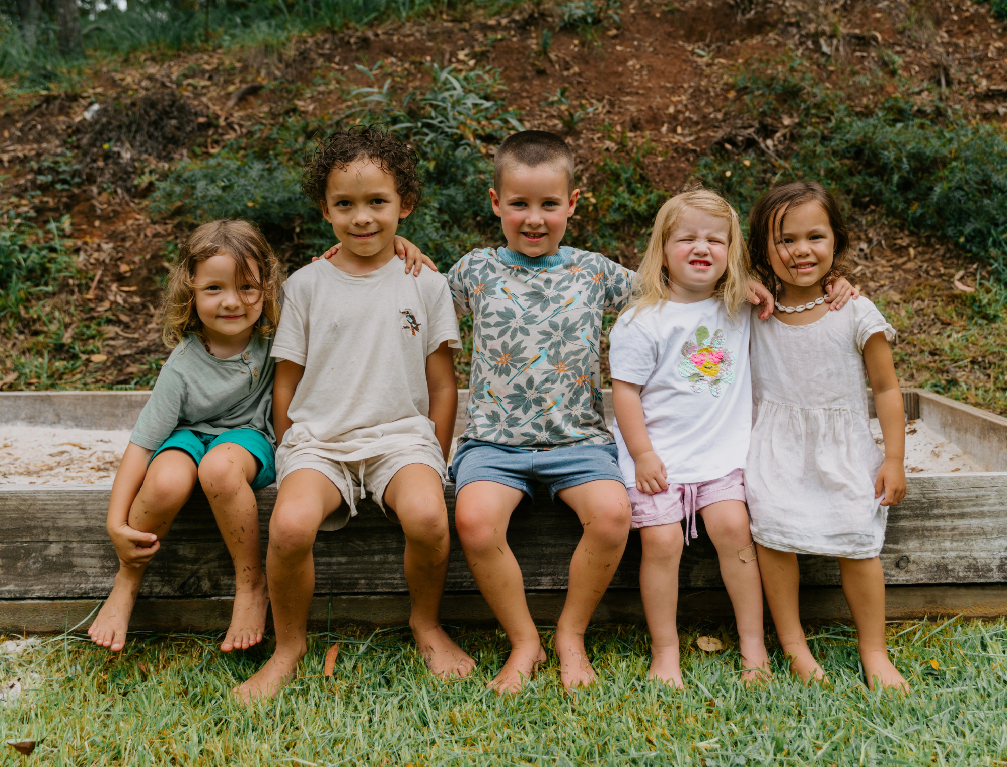Five diverse children sitting together outdoors, smiling and looking at the camera.