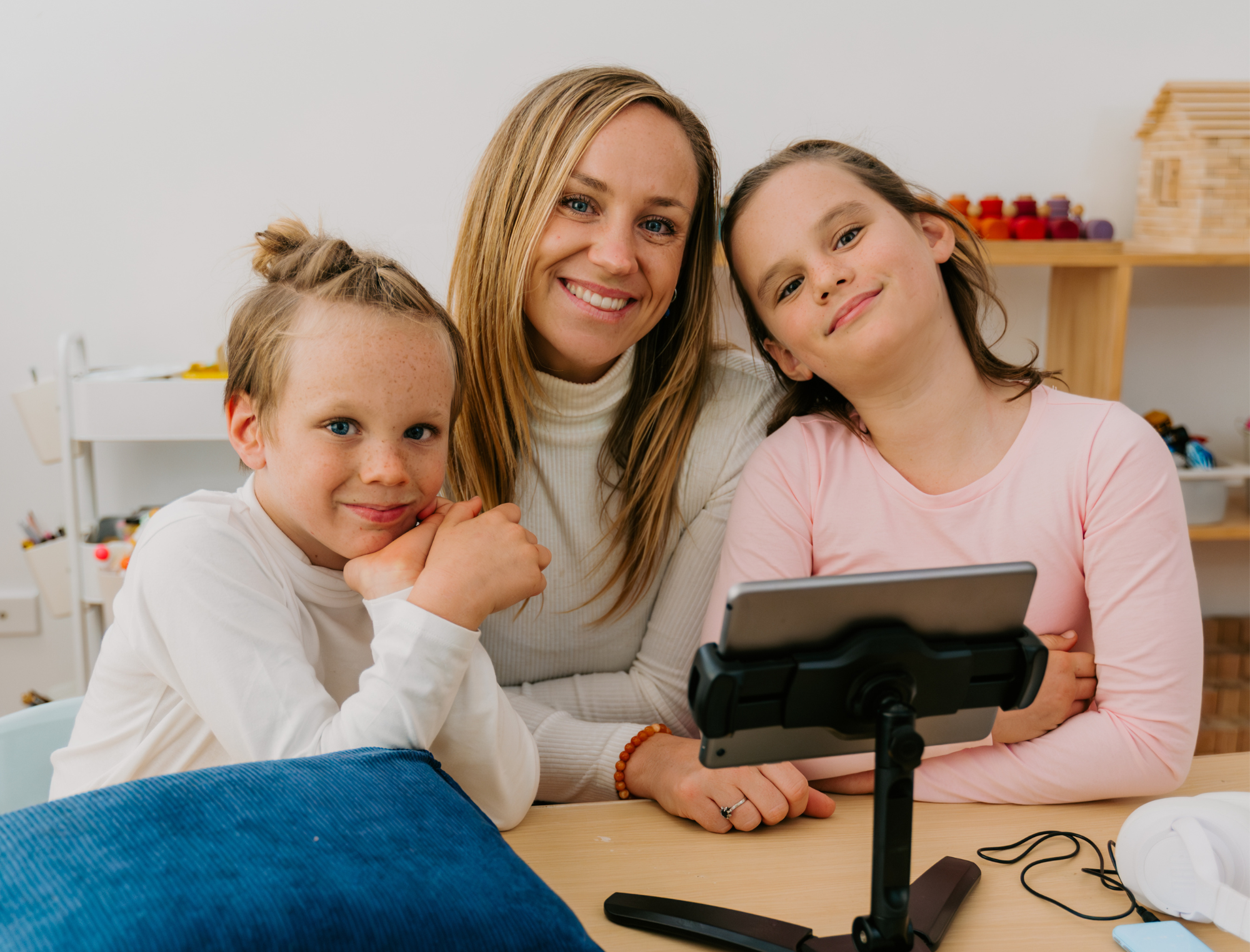 Teacher and two children smiling while looking at a tablet in a classroom.